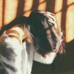 woman leans on wall in white fur jacket docking her head while holding it using her leaf hand